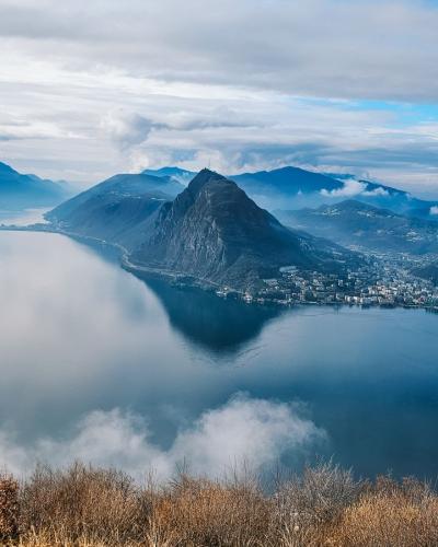 Aerial view of Lake Lugano surrounded by mountains and clouds, offering breathtaking scenery.